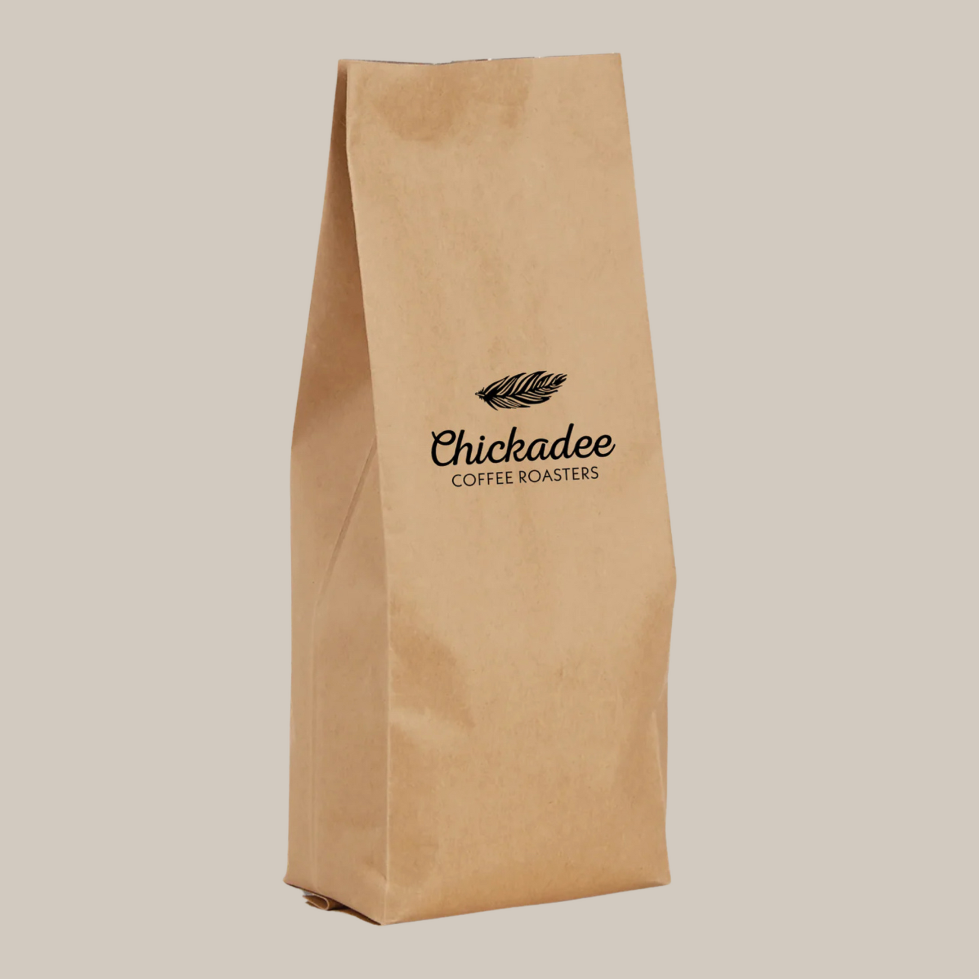 A plain brown paper bag with the Chickadee Coffee Roasters logo and a feather in black, set against light beige, featuring Guatemala Huehuetenango coffee with toffee flavor notes.