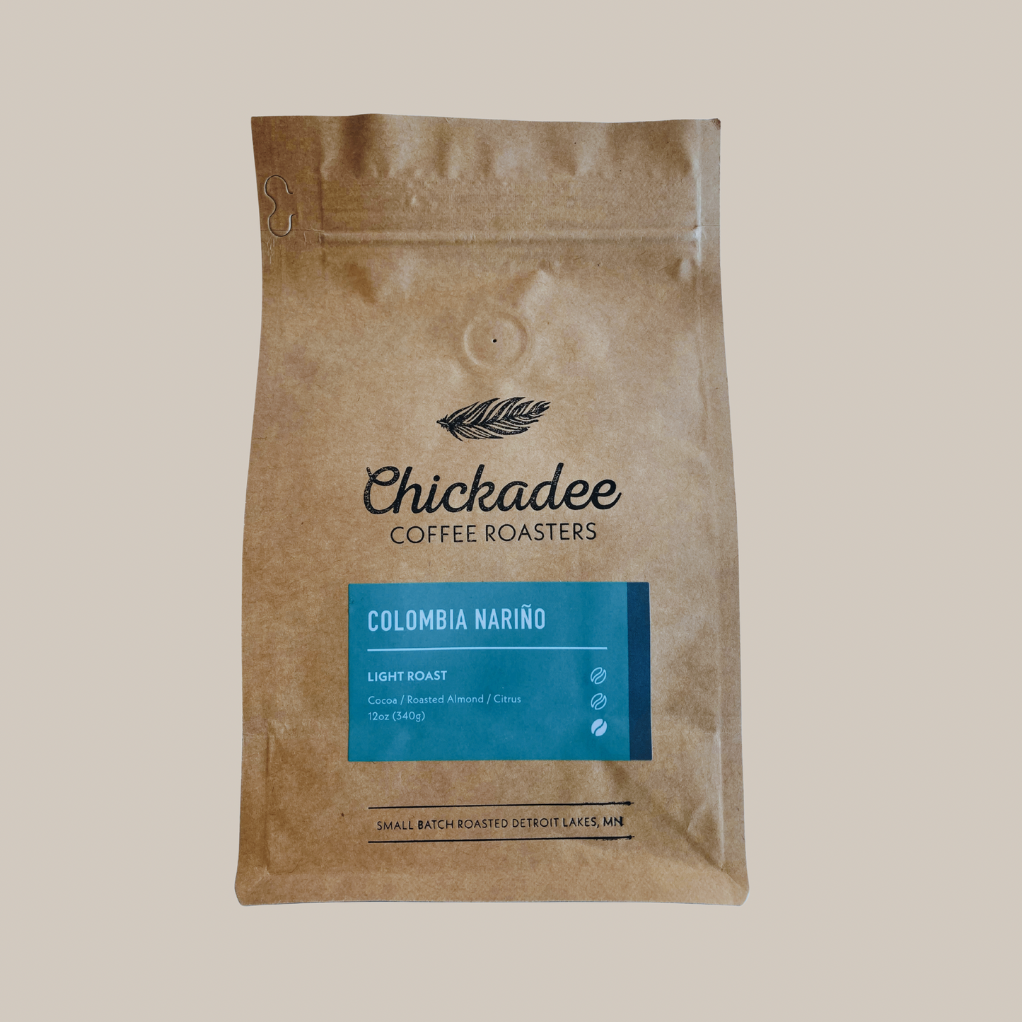A brown bag of Chickadee Coffee Roasters Colombia Nariño sits on a beige background, showcasing its blue light roast label and notes of roasted almond and citrus.
