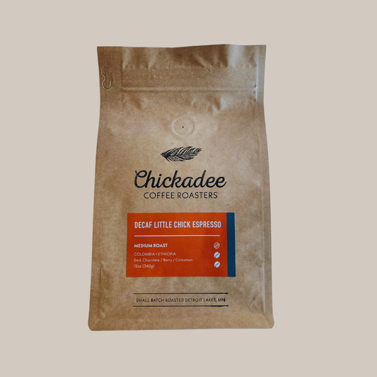 A sealed brown bag of Chickadee Coffee Roasters’ Variety Bundle (4 Pack) stands upright, featuring a blue and orange label with tasting notes and origin details, set against a plain background.