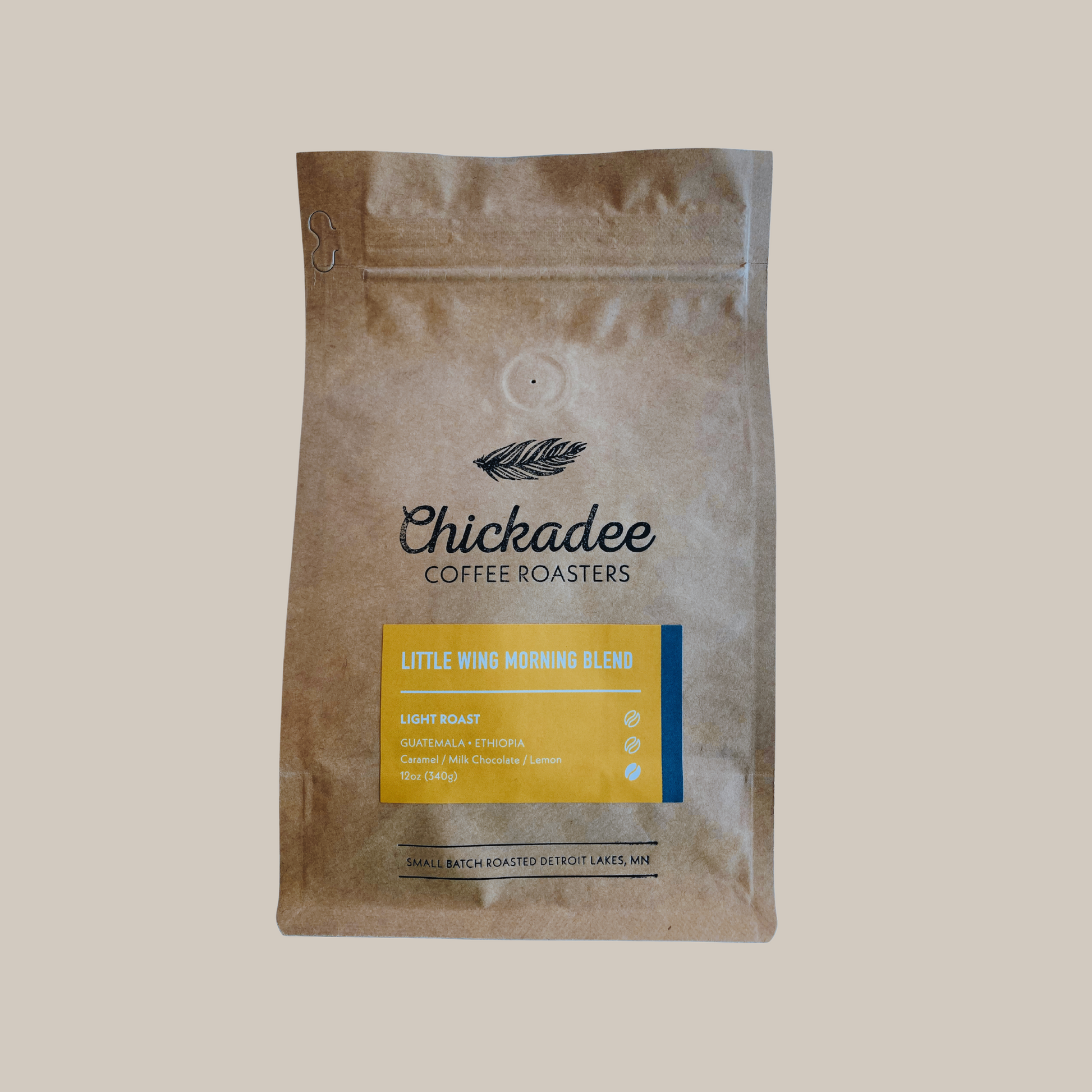 A brown bag from Chickadee Coffee Roasters’ Variety Bundle (4 Pack) displays a yellow label with blend details and a feather above the brand name on simple packaging.